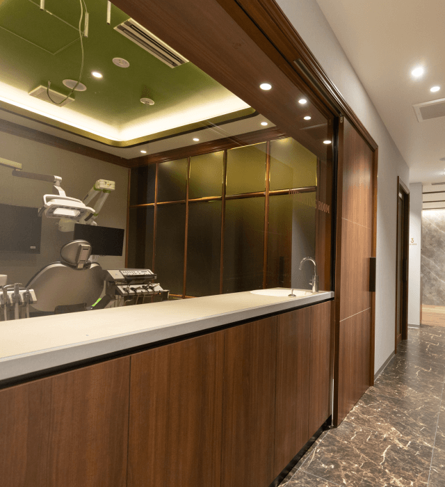 木目とガラスでデザインされた診療室前の廊下と、ガラス越しに見える治療ユニット