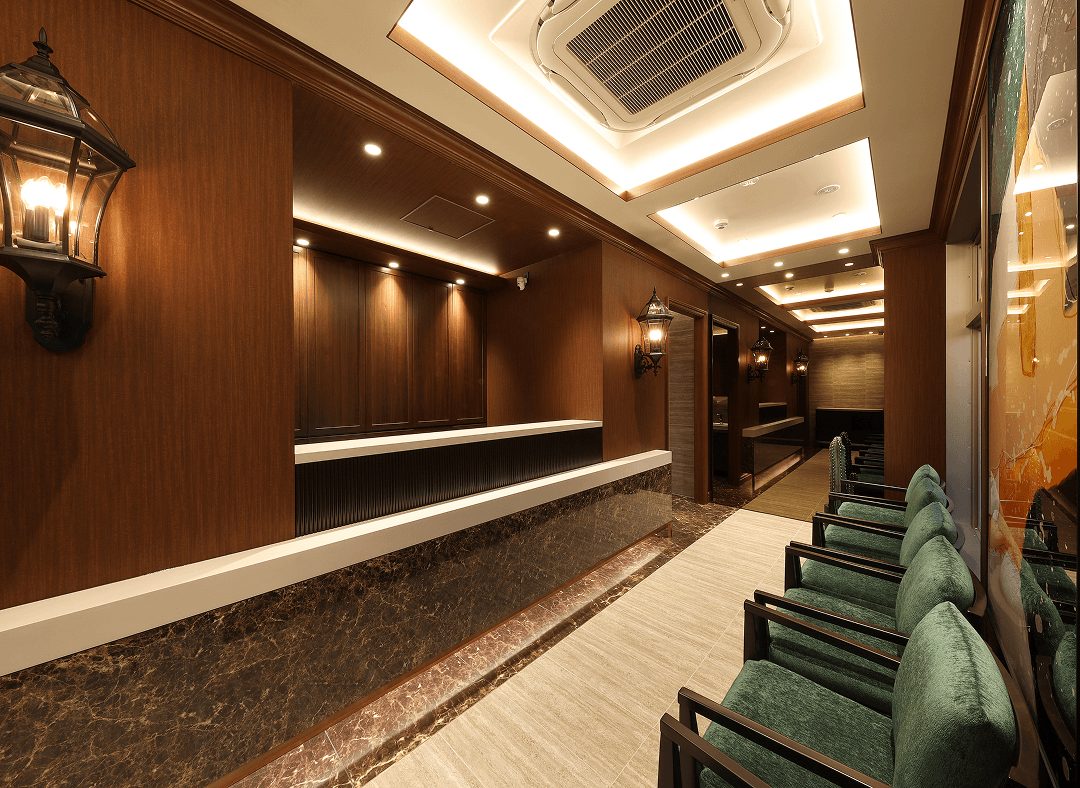 木目調の受付カウンターと緑色の椅子が並ぶ、落ち着いた雰囲気のクリニック待合室